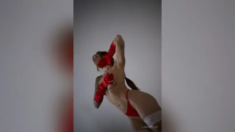 Athletic woman in red lingerie posing confidently against a minimalist grey studio background.