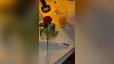 A single red rose resting on a white napkin next to a glass of orange juice on a marble restaurant table.