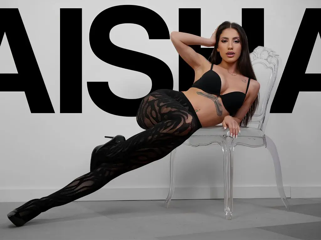 Stylish woman in black lace lingerie and patterned tights posing confidently on a clear chair against a logo wall.