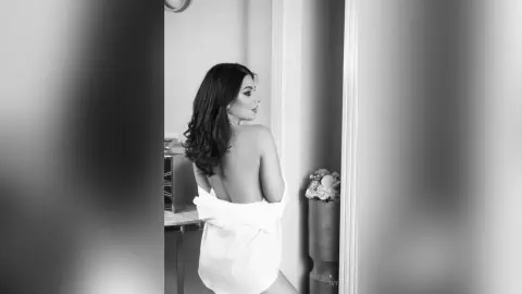 Elegant woman in a white silk robe looking away in a moody, minimalist black and white indoor setting.