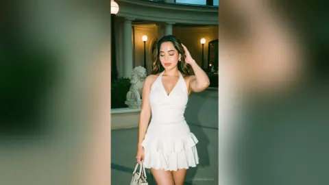 LilianMendoza poses outdoors at night wearing a white plunging halter-neck ruffle dress with her hand in her hair.