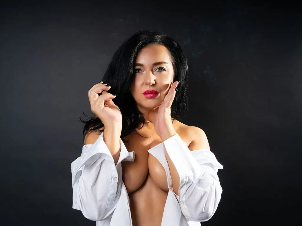 Beautiful woman with dark hair in an open white shirt posing against a black background with a moody vibe.