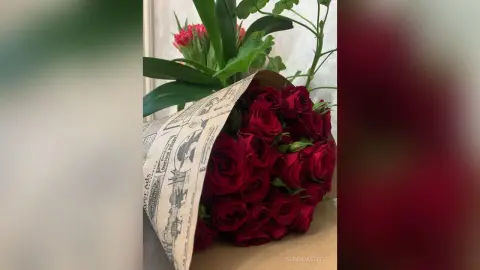 A romantic bouquet of deep red roses wrapped in vintage newsprint paper on a wooden surface.