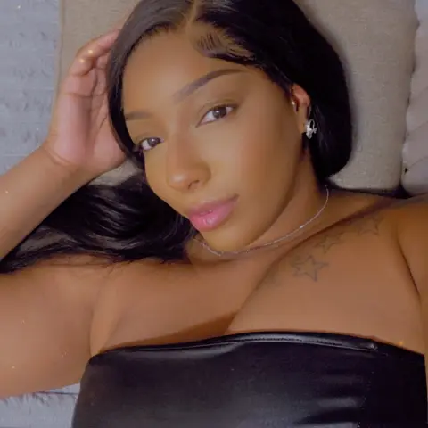 Beautiful Black woman in a black strapless top relaxing on a bed with a soft, glowing aesthetic.