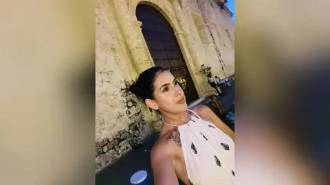 Young woman in a white halter top smiling in front of a historic stone building at night.