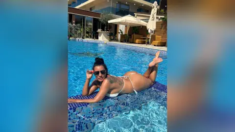 MissyJolie lies on the edge of a blue tiled swimming pool wearing a white bikini and sunglasses.