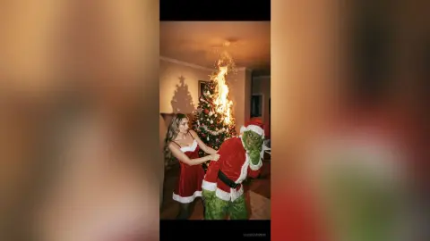Woman in red satin dress hugging a person in a Grinch costume during a festive indoor Christmas celebration.