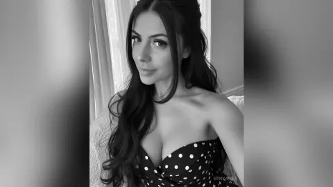 Smiling woman in a polka dot strapless top posing for a moody black and white portrait indoors.