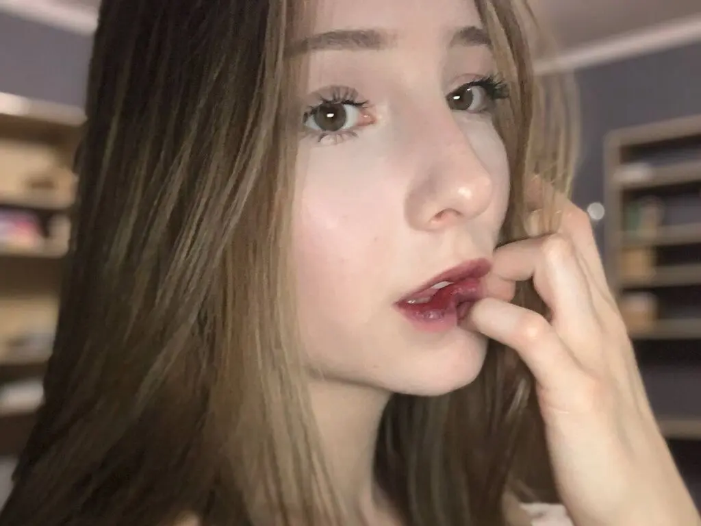 Close-up portrait of a young woman with long brown hair and red lipstick in a soft, natural indoor setting.