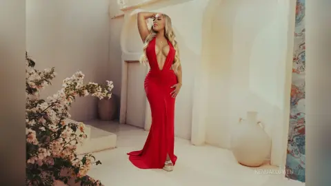 Elegant woman in a plunging red evening gown posing in a bright, minimalist Mediterranean-style studio.