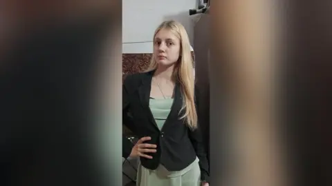 GeorgineAragan stands wearing a black blazer over a light green top with her long blonde hair down.