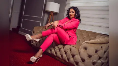 Elegant woman in a bright pink suit sitting on a luxury velvet sofa in a stylish modern room.