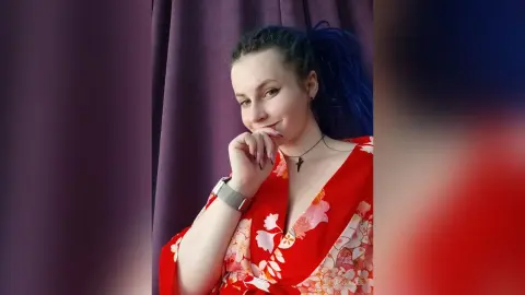 Smiling young woman in a red floral kimono posing against a purple curtain backdrop.