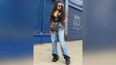 Stylish woman in black crop top and wide-leg jeans posing against a blue shuttered wall in urban street style.