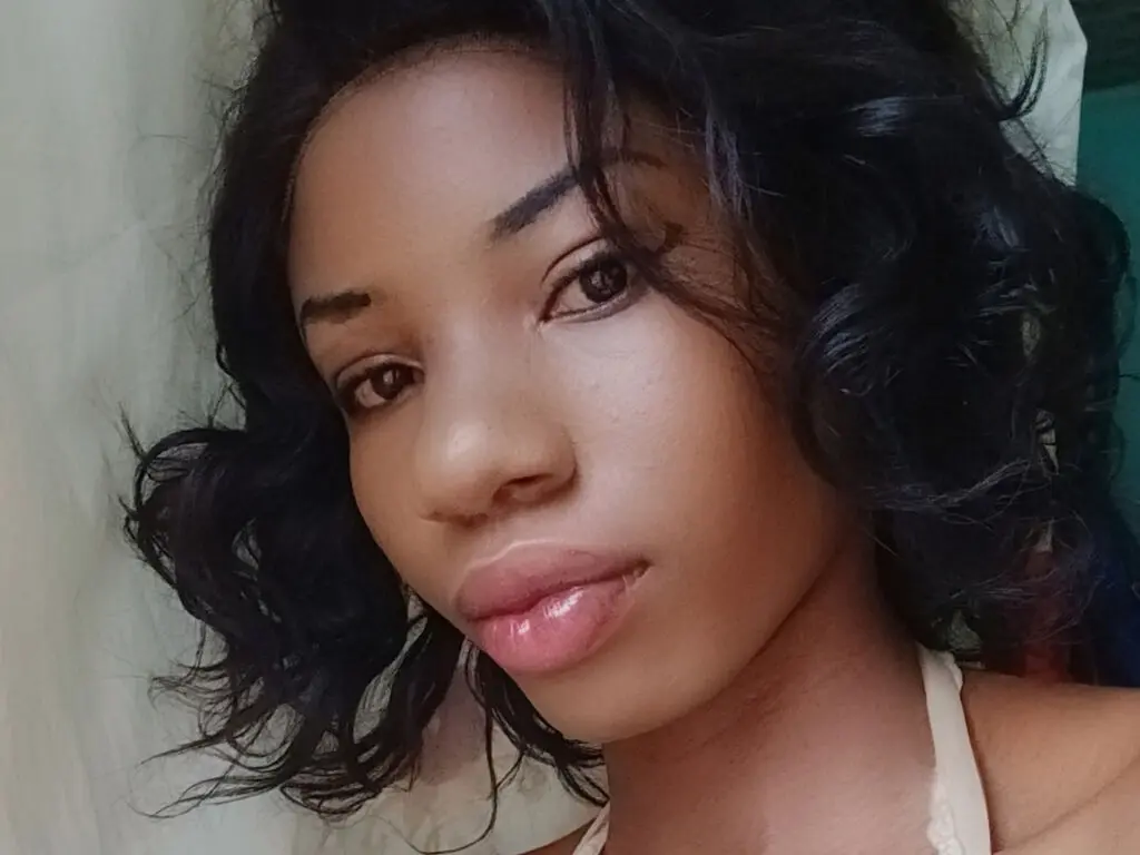 Close-up portrait of a young woman with wavy black hair and natural makeup in a soft indoor setting.