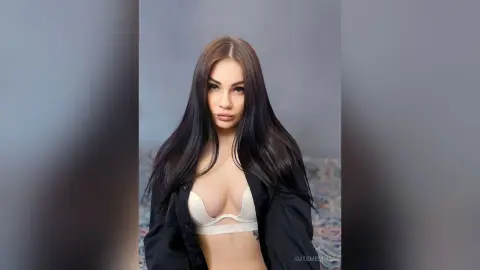 CutemEmma poses looking at the camera, wearing an open black shirt over a white bra, showing her cleavage and long dark hair.