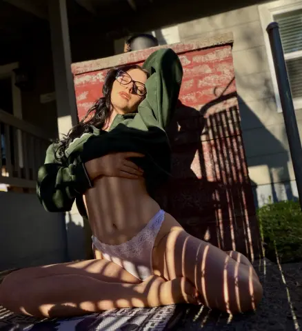 Young woman in glasses and white lace lingerie relaxing in sunlight outdoors.