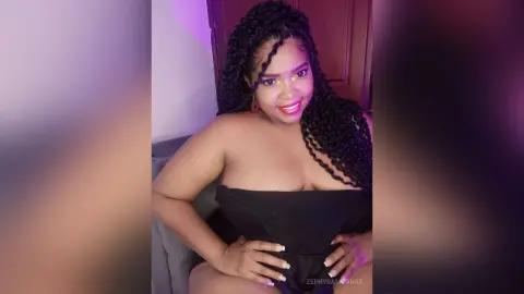 Smiling Black woman in a black strapless top posing indoors with soft purple lighting.
