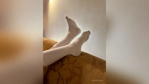 Close-up of feet in white socks resting on a gold patterned sofa in a cozy, dimly lit room.