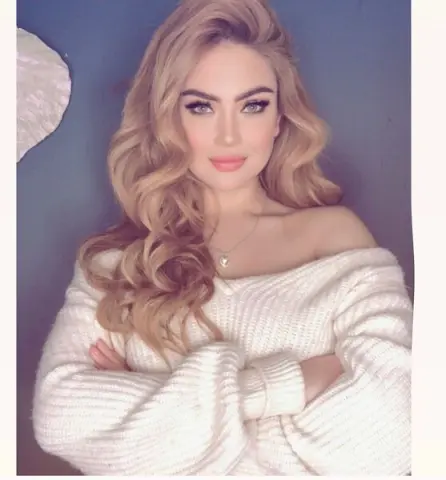 Blonde woman in a cozy white knit sweater posing with a soft, dreamy expression against a blue background.
