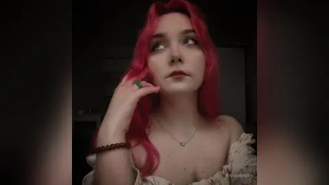 Young woman with pink hair in a white floral dress looking away in a moody, dimly lit indoor setting.