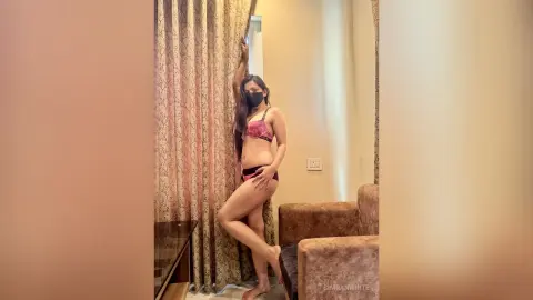 Young woman in a pink patterned bikini bra posing by patterned curtains in a bright, modern room.