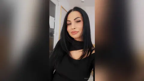 Smiling woman with long black hair wearing a black off-the-shoulder top in a bright indoor setting.