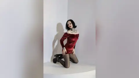 KailaTaylor poses kneeling in a red velvet off-the-shoulder dress and black tights against a plain white background.