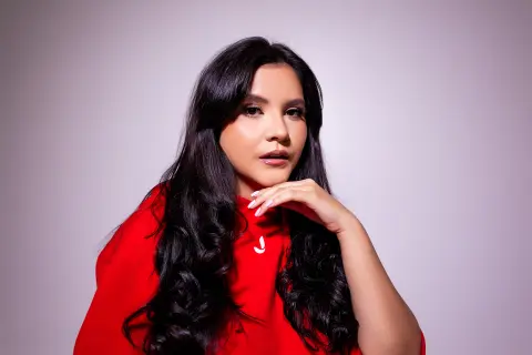 Elegant woman in a red sweater posing with long wavy hair against a soft studio background.