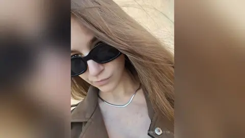 IngridBeckton wears black sunglasses and a silver necklace, posing with her long brown hair down in a brown jacket.
