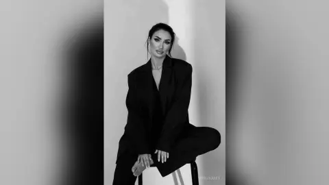 AnnaKarev poses in a black blazer and trousers with her dark hair pulled back against a plain background.