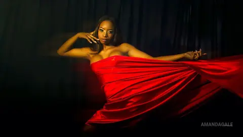 Elegant woman in a flowing red silk dress posing against a dark backdrop with a dramatic, moody atmosphere.