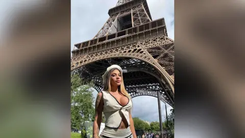 Stylish woman in a white sleeveless top posing in front of the Eiffel Tower in Paris on a sunny day.