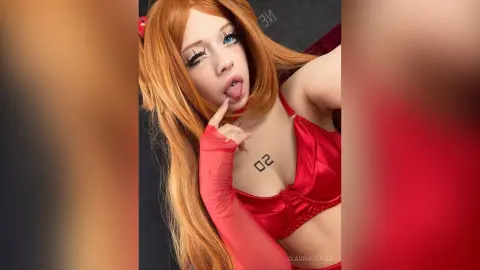 Cosplayer in red lingerie and orange wig posing with a playful expression in a studio setting.