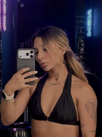 Young woman in black sports bra taking a mirror selfie in a dimly lit gym setting.