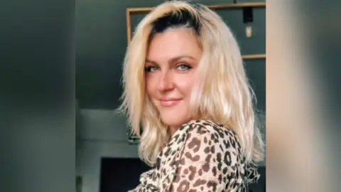 Smiling blonde woman in a leopard print blouse posing in a bright indoor setting.
