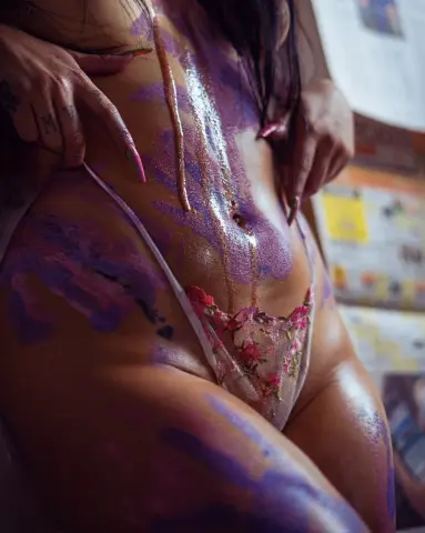 Woman in floral lace lingerie with shimmering body paint in a soft, intimate indoor setting.