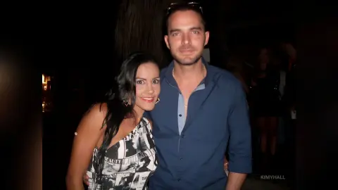 Smiling couple in elegant evening attire posing together at a dimly lit night event.