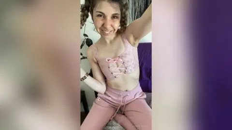 Smiling woman in pink lace sports bra and matching leggings posing in a cozy indoor setting.