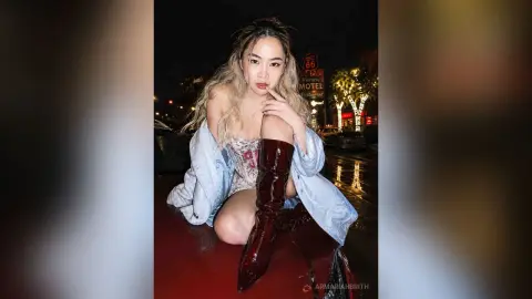 Stylish woman in a floral corset and tall burgundy boots posing at night near a vintage motel sign.