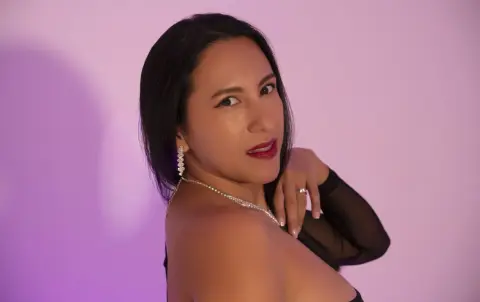Elegant woman in a black dress and diamond jewelry posing against a soft purple background.