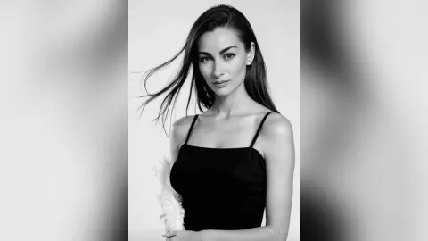 Elegant woman in a black sleeveless dress with flowing hair in a minimalist black and white studio portrait.