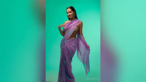 Elegant woman in a flowing purple silk saree posing against a teal background with a graceful mood.