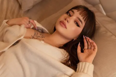 Young woman in a cozy white sweater relaxing on a bed with a peaceful, dreamy expression.
