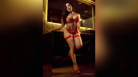 Glamorous woman in red lace lingerie and stockings posing in a moody, dimly lit luxury bathroom.