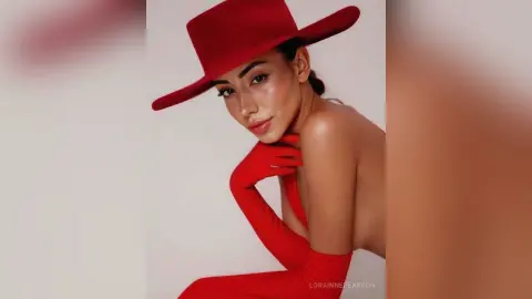 Elegant woman in a red wide-brimmed hat and matching gloves posing against a minimalist studio background.