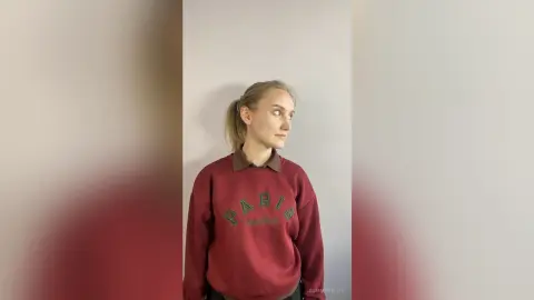 Young woman in a burgundy Paris graphic sweatshirt posing against a neutral wall with a calm expression.