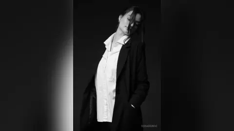 Elegant woman in a white shirt and black blazer posing in a moody black and white studio portrait.