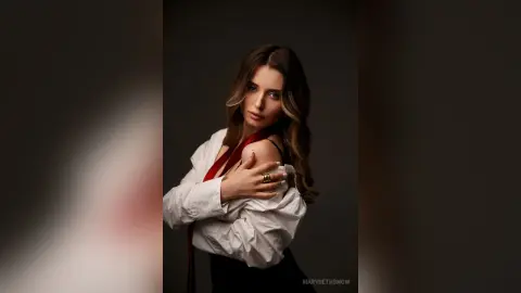 Elegant woman in a white blouse and red ribbon posing with a moody, sophisticated expression against a dark backdrop.
