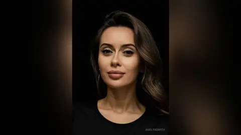 Portrait of a smiling woman with wavy brown hair wearing a black top against a dark moody background.